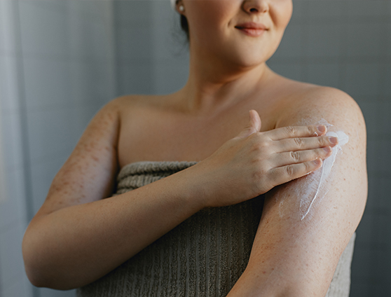 A woman applying lotion to the upper arm